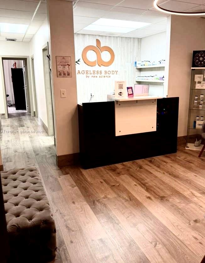 A reception area features a black desk, wood-look flooring, and a branded wall sign — 2500 E Hallandale Beach Blvd, Hallandale Beach FL 33009, HALLANDALE BEACH, FL