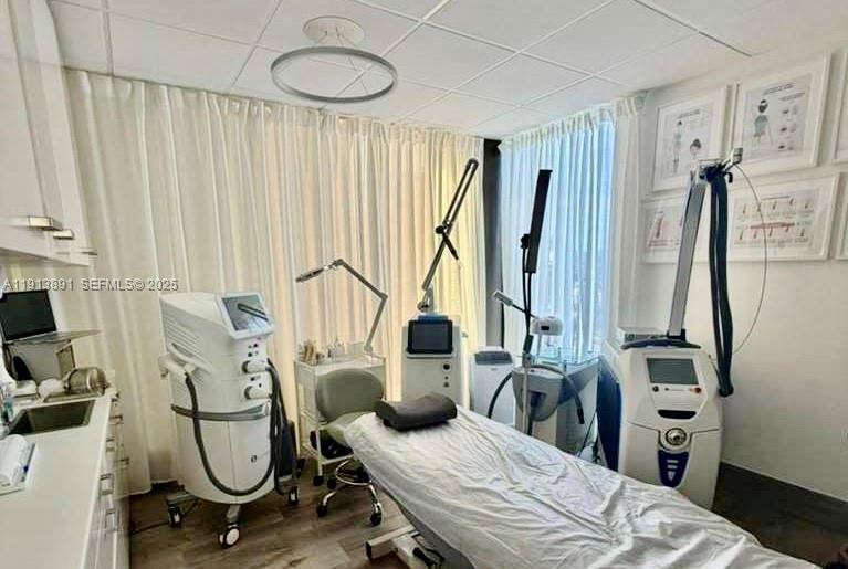A medical aesthetic treatment room features a procedure bed, multiple laser machines, and white curtains — 2500 E Hallandale Beach Blvd, Hallandale Beach FL 33009, HALLANDALE BEACH, FL
