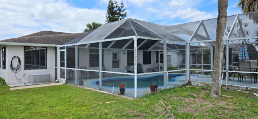 A backyard view of a house with a screened-in pool enclosure and a grassy lawn — 5445 SANDY HILL DRIVE, ORLANDO, FL