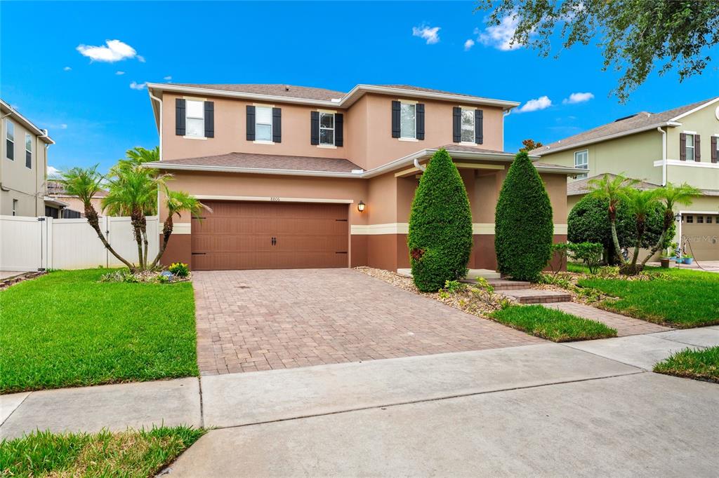 A two-story suburban house features a brown stucco exterior, a paved driveway, and manicured landscaping — 8806 TATARA STREET, ORLANDO, FL