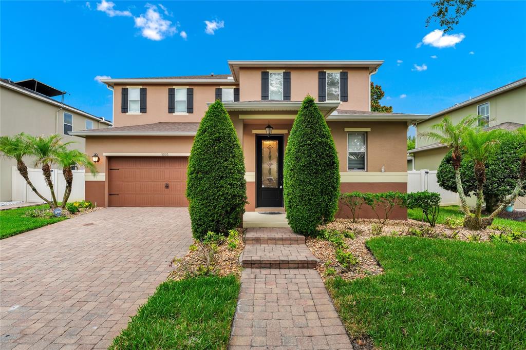 A two-story suburban house features a brown garage, a paved walkway, and two tall shrubs — 8806 TATARA STREET, ORLANDO, FL