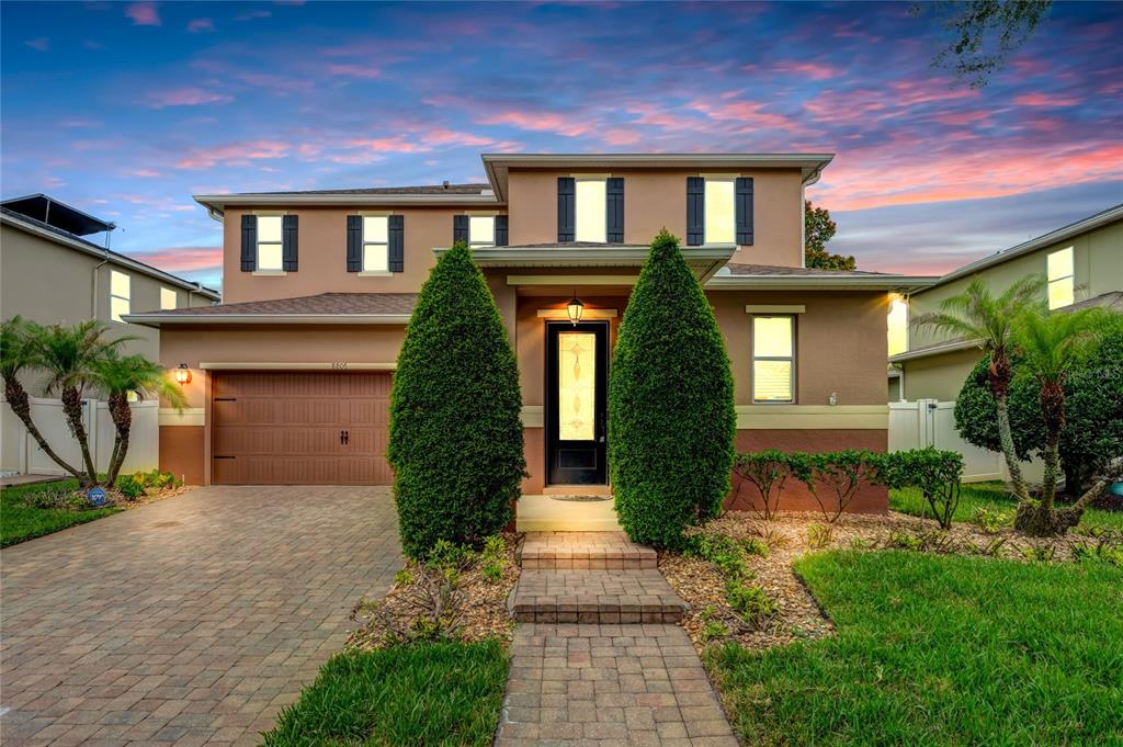 A two-story suburban house features a tan stucco exterior, a paved driveway, and two large shrubs — 8806 TATARA STREET, ORLANDO, FL