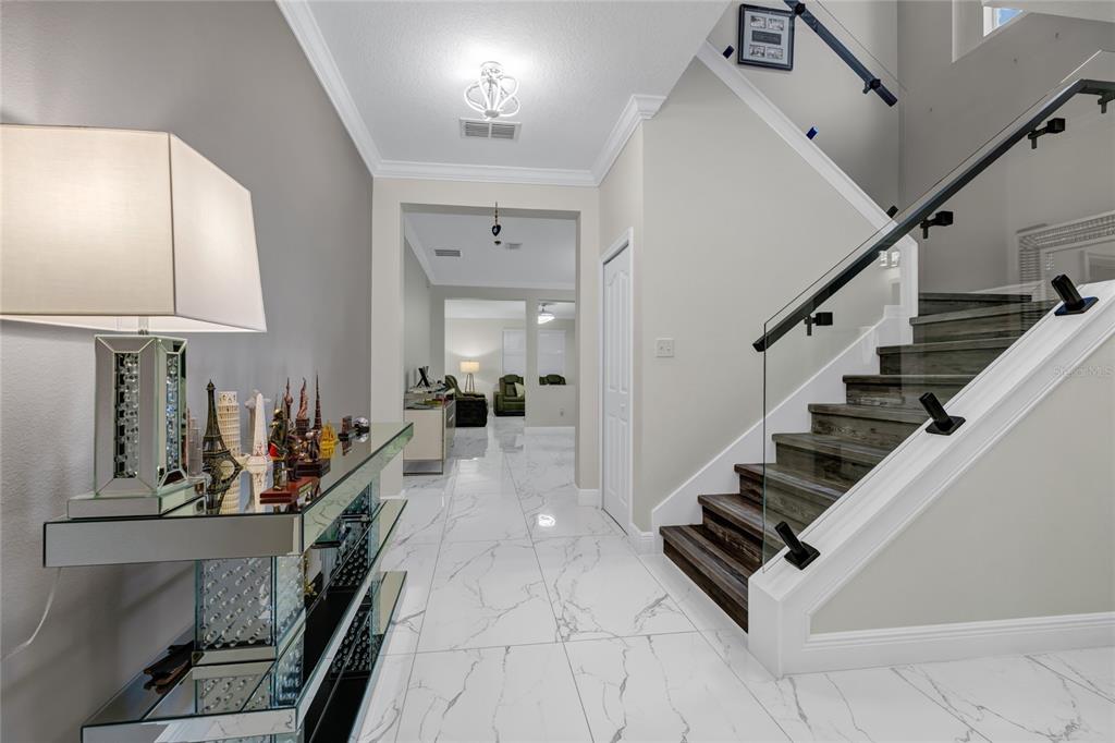 A foyer with white marble tile floors, a glass-railed staircase, and a mirrored console table — 8806 TATARA STREET, ORLANDO, FL