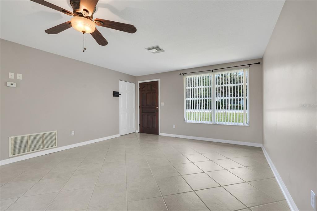 A living room with light tile flooring, a ceiling fan, and a dark wood front door — 520 N LACY CIRCLE, DELTONA, FL