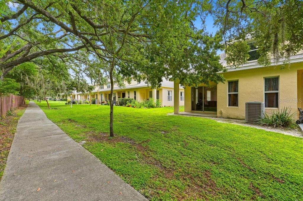 A view of a grassy backyard with a concrete walkway and a yellow townhouse exterior — 2446 TEMPLE GROVE LANE, KISSIMMEE, FL