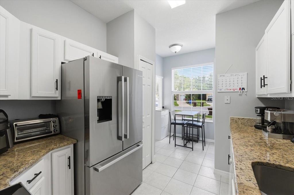 A kitchen features white cabinets, granite countertops, a stainless steel refrigerator, and a breakfast nook — 2446 TEMPLE GROVE LANE, KISSIMMEE, FL
