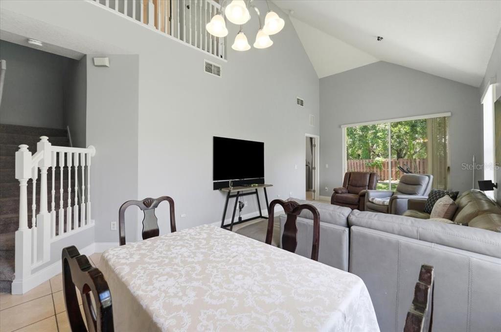 A dining area with a table leads into a living room with vaulted ceilings — 2446 TEMPLE GROVE LANE, KISSIMMEE, FL
