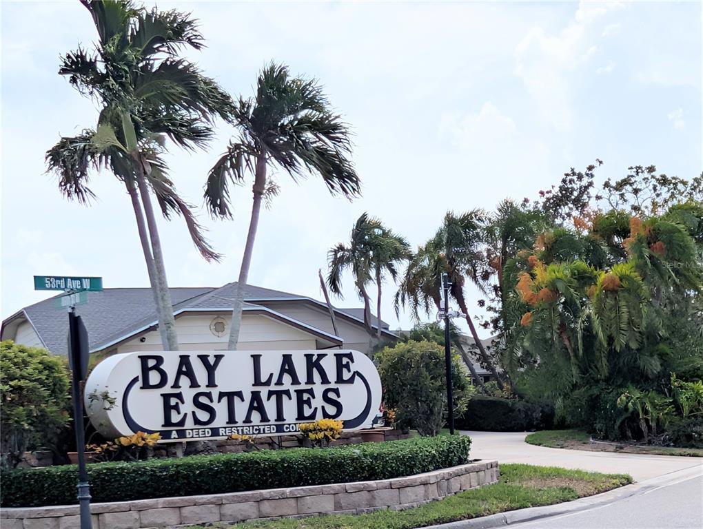 A sign for Bay Lake Estates stands in front of palm trees and a house — 8707 51ST AVENUE W, BRADENTON, FL