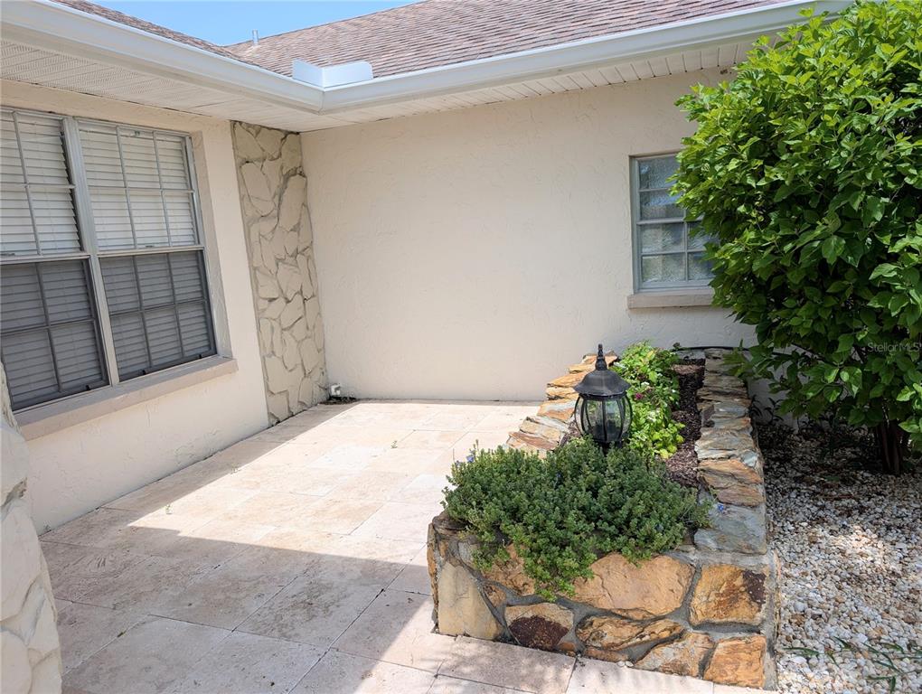 A stone-walled planter sits on a tiled patio next to a house exterior — 8707 51ST AVENUE W, BRADENTON, FL