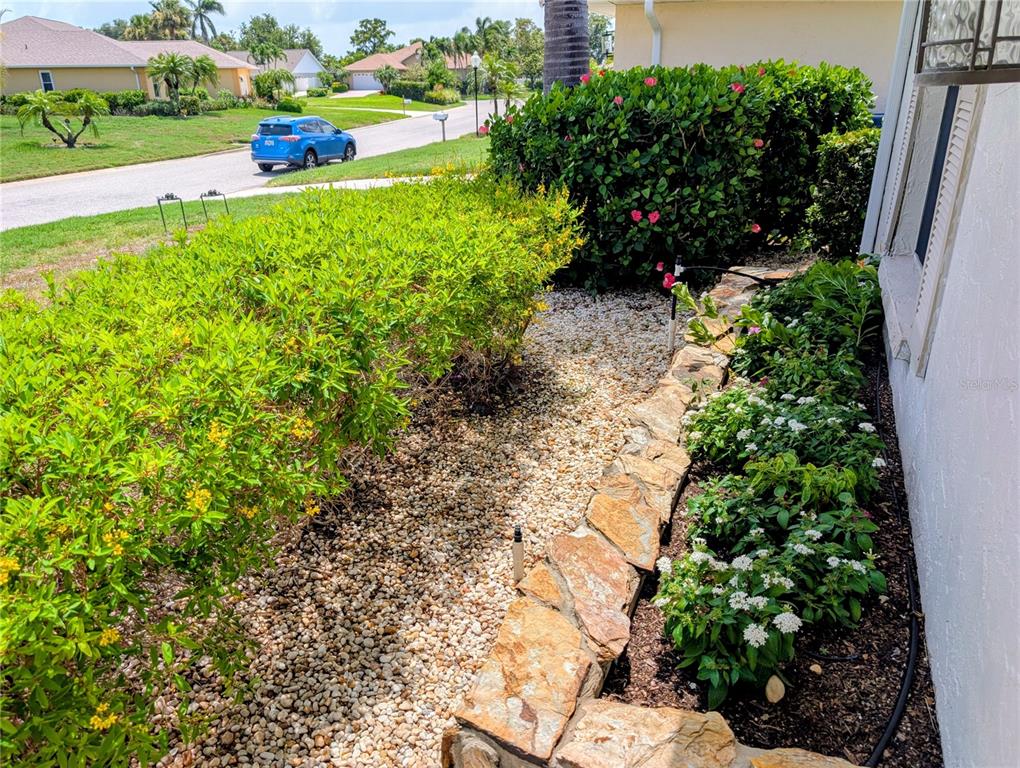 A stone retaining wall borders a gravel garden bed with shrubs and flowers beside a house — 8707 51ST AVENUE W, BRADENTON, FL