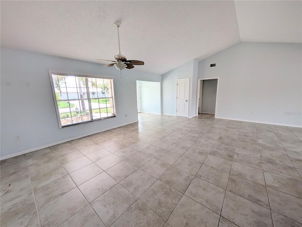An empty room with light blue walls, large windows, a ceiling fan, and tiled floors — 8707 51ST AVENUE W, BRADENTON, FL