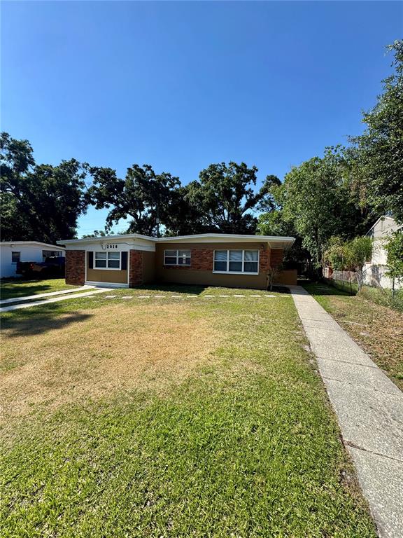 A single-story house with a brick facade, a concrete driveway, and a large front lawn — 2016 E CRENSHAW STREET, TAMPA, FL