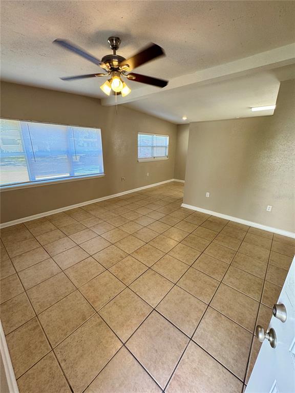 An empty room with tan tile flooring, a ceiling fan, and a partial partition wall — 2016 E CRENSHAW STREET, TAMPA, FL
