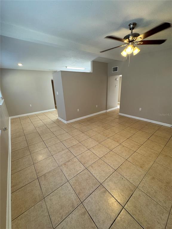 A kitchen with white cabinets, stainless steel appliances, and tile flooring opens to a room — 2016 E CRENSHAW STREET, TAMPA, FL