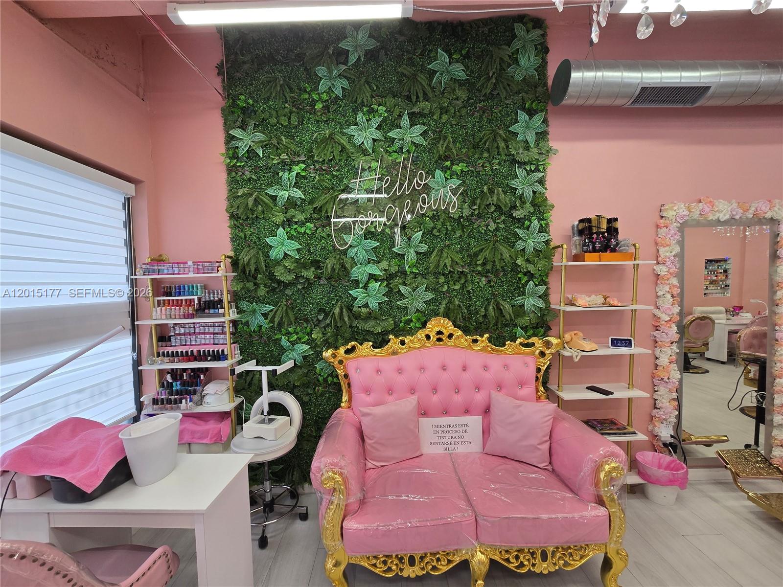 A pink salon features a tufted gold-trimmed loveseat against a green wall with neon signage — MIAMI, FL