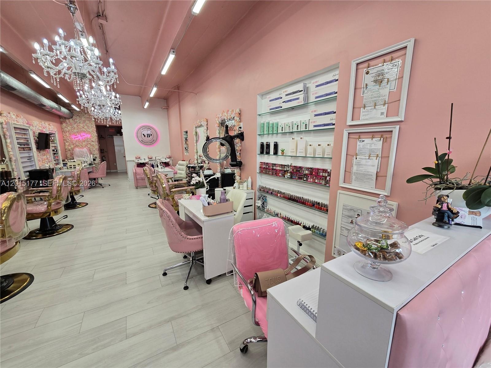 A bright pink beauty salon features crystal chandeliers, nail stations, and product display shelving — MIAMI, FL
