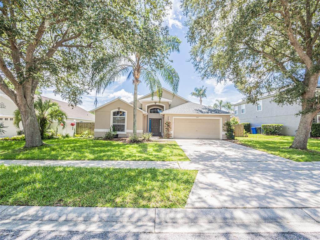 A single-story suburban house with a tan exterior, a two-car garage, and mature trees — 2843 STRAND CIRCLE, OVIEDO, FL