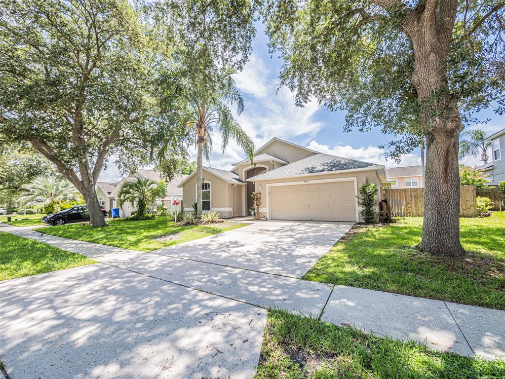 A single-story suburban house with a beige exterior, two-car garage, and mature trees — 2843 STRAND CIRCLE, OVIEDO, FL