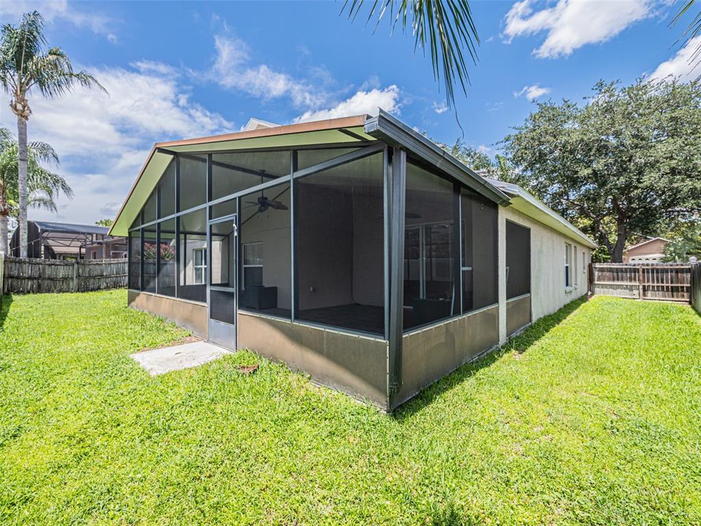 A screened-in patio with a metal frame sits in a grassy backyard under a blue sky — 2843 STRAND CIRCLE, OVIEDO, FL