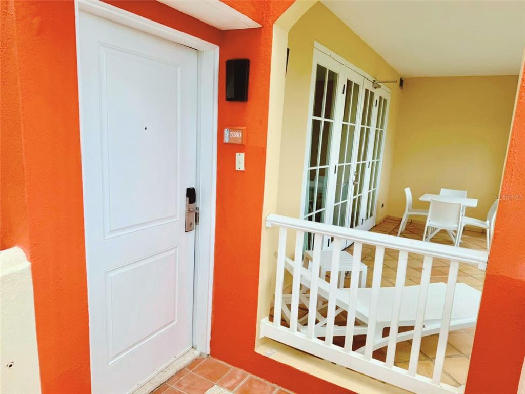 A white front door with a number plate sits beside a balcony with white furniture — 1000 LAS CASITA I, EL CONQUISTADOR AVE. UNIT 5380, FAJARDO, PR
