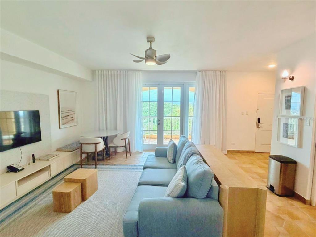 A living room features a blue sofa, a television, a dining area, and balcony doors — 1000 LAS CASITA I, EL CONQUISTADOR AVE. UNIT 5380, FAJARDO, PR