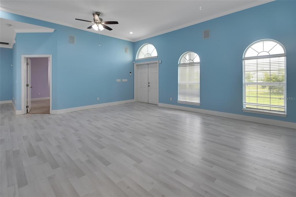 A spacious room with light blue walls, light wood flooring, arched windows, and a ceiling fan — 2590 ERENA DRIVE, NEW SMYRNA BEACH, FL