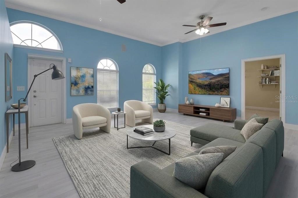 This virtually staged living room features light blue walls, arched windows, and a gray sectional sofa — 2590 ERENA DRIVE, NEW SMYRNA BEACH, FL