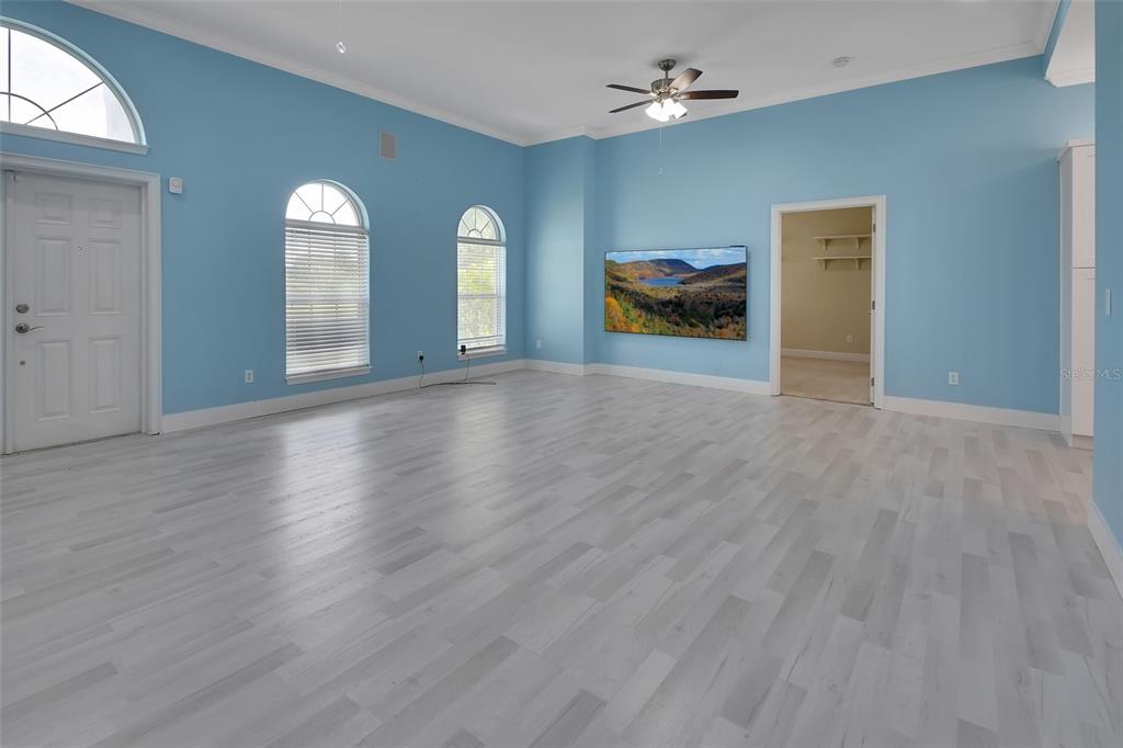A spacious room with light blue walls, light wood flooring, arched windows, and a television — 2590 ERENA DRIVE, NEW SMYRNA BEACH, FL