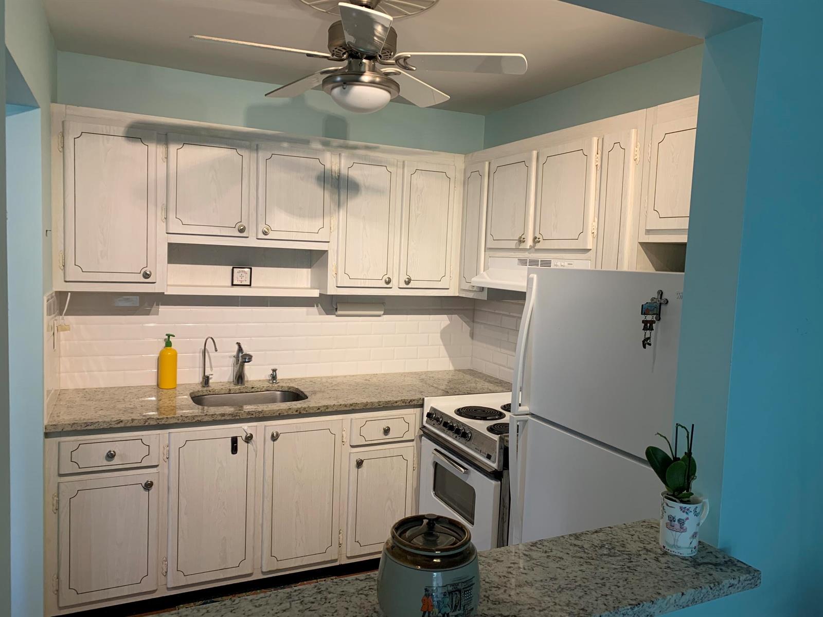 A kitchen features white cabinets, granite countertops, a subway tile backsplash, and a white stove — 100 S South Boulevard # 1c, Boynton Beach FL 33435, BOYNTON BEACH, FL