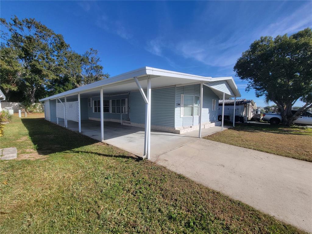 A light blue manufactured home features a long covered carport and a concrete driveway — 36603 JODI AVENUE, ZEPHYRHILLS, FL