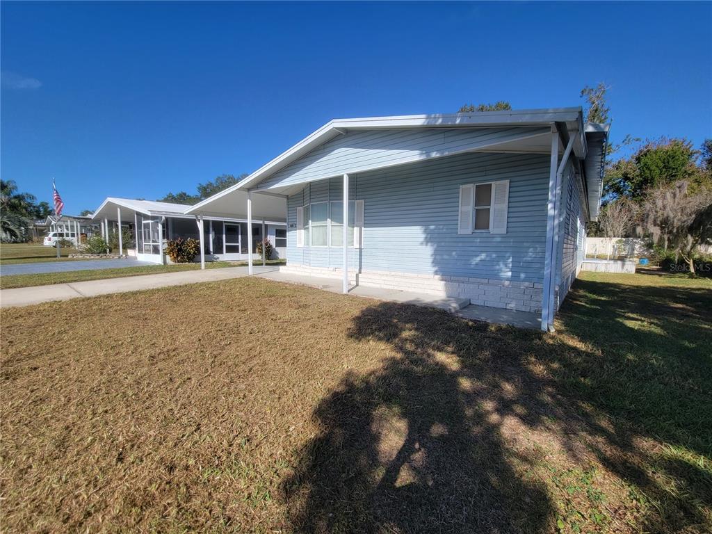 A light blue mobile home with a carport and a front lawn under a clear sky — 36603 JODI AVENUE, ZEPHYRHILLS, FL