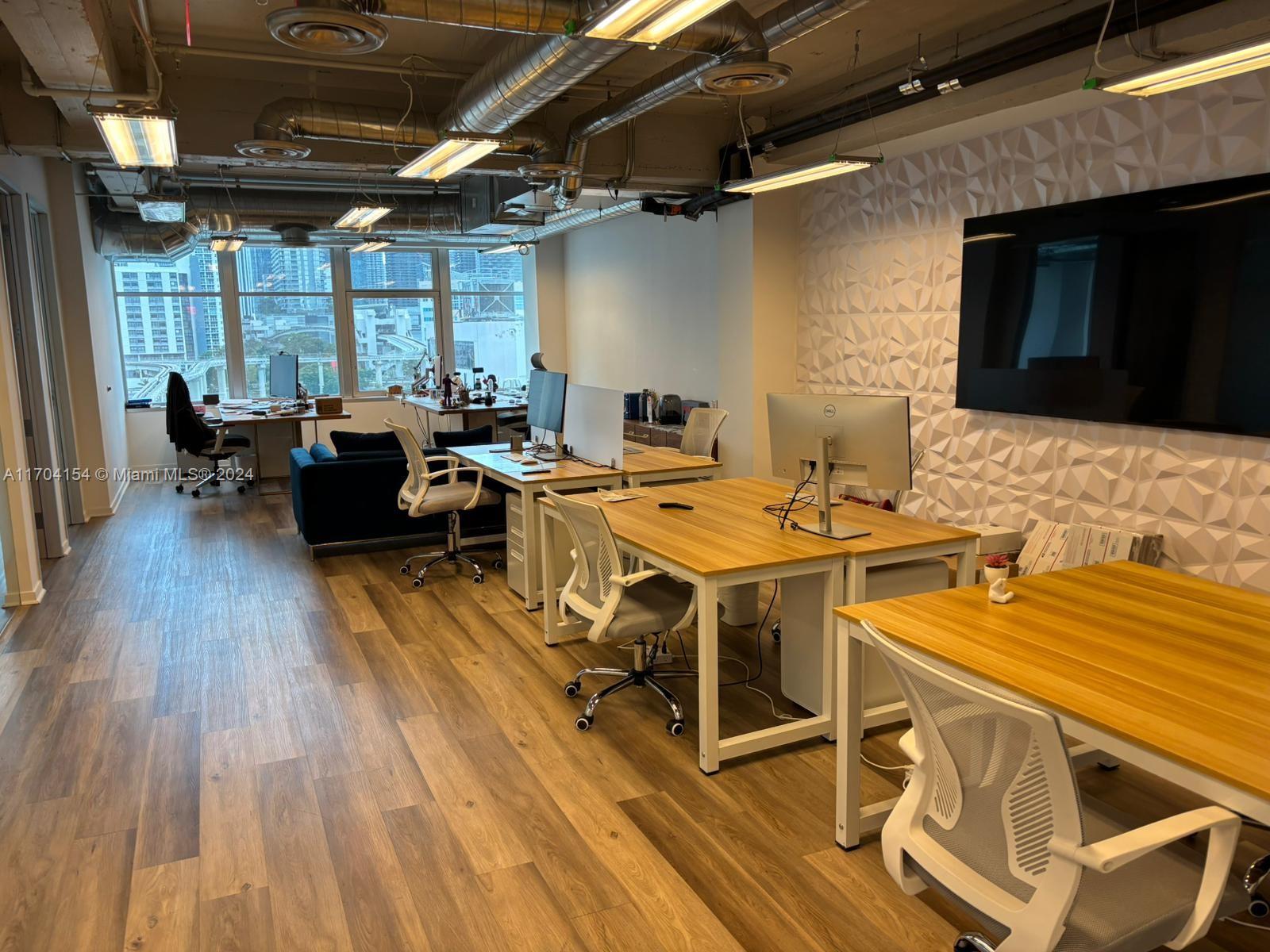 An office space features multiple desks, white chairs, wood flooring, and a textured accent wall — 14 NE 1st Ave, Miami FL 33132, MIAMI, FL