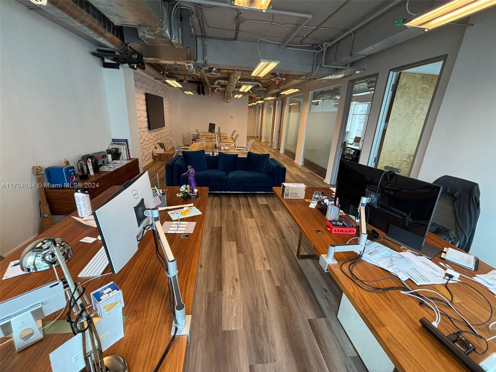This office space features two wooden desks, a blue sofa, and an exposed ceiling — 14 NE 1st Ave, Miami FL 33132, MIAMI, FL