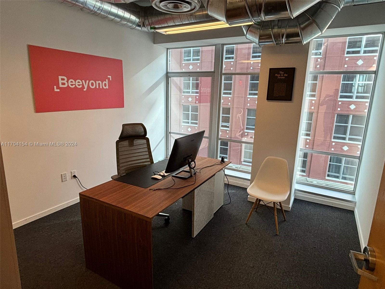 A modern office features a wooden desk, a mesh chair, and large windows overlooking buildings — 14 NE 1st Ave, Miami FL 33132, MIAMI, FL