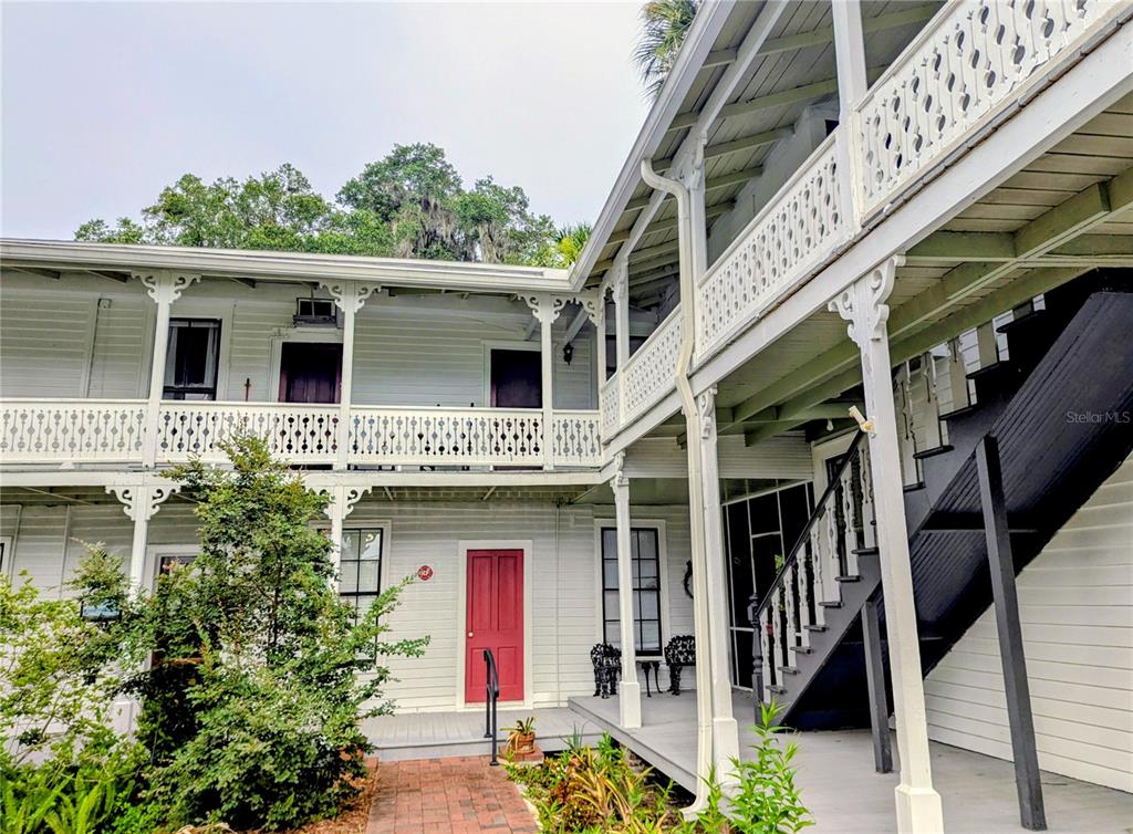A two-story white building features a wooden balcony, a red door, and an exterior staircase — 6635 SE 221ST STREET UNIT 3, HAWTHORNE, FL