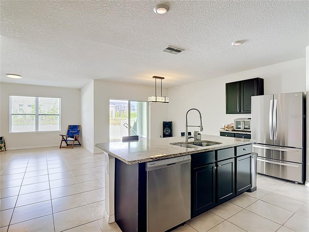 A kitchen features a granite-topped island, stainless steel appliances, and dark cabinetry — 2352 WHITE POPPY DRIVE, KISSIMMEE, FL