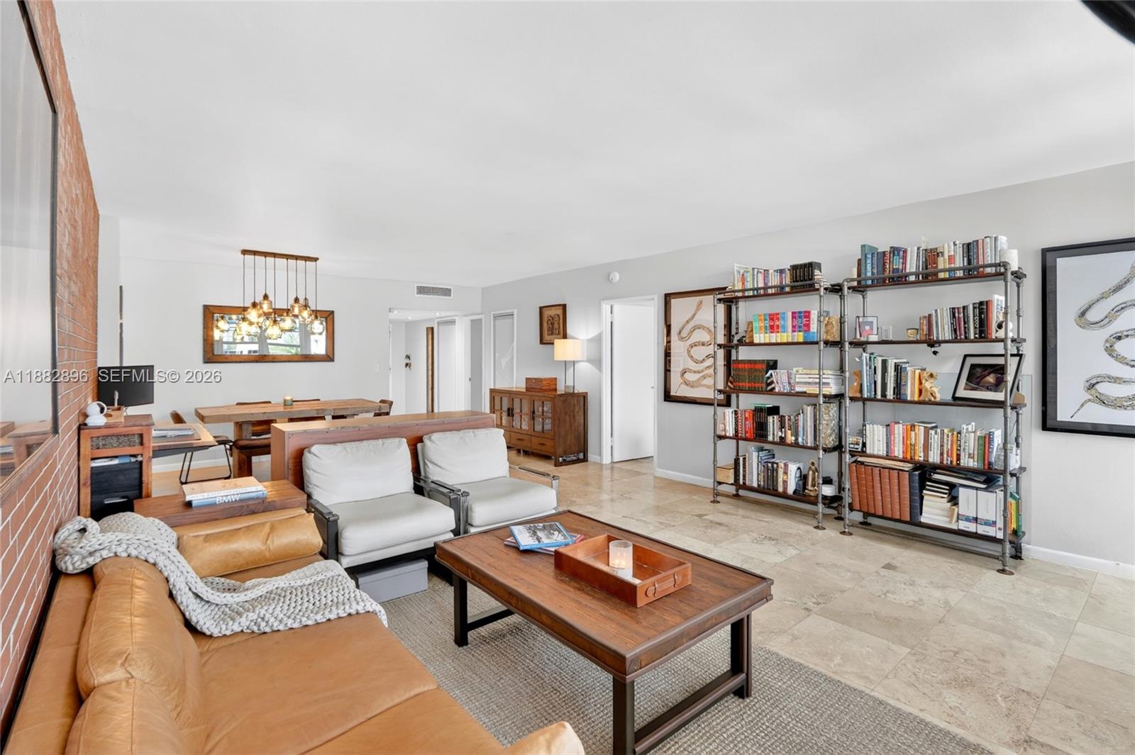 A living room features a leather sofa, two armchairs, a wooden coffee table, and bookshelves — 5700 Collins Ave # 3M, Miami Beach FL 33140, MIAMI BEACH, FL