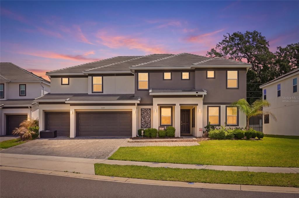 A two-story suburban house with a three-car garage and a paved driveway at sunset — 2437 SHANTI DRIVE, KISSIMMEE, FL