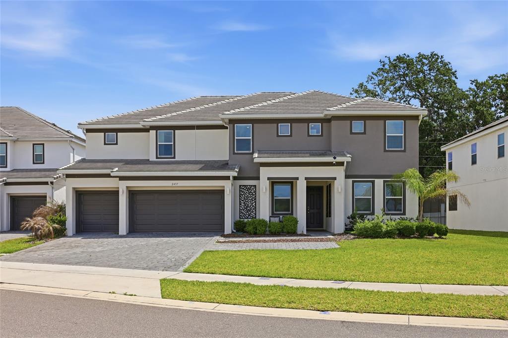 A two-story suburban house with a gray garage, stucco exterior, and a paved driveway — 2437 SHANTI DRIVE, KISSIMMEE, FL