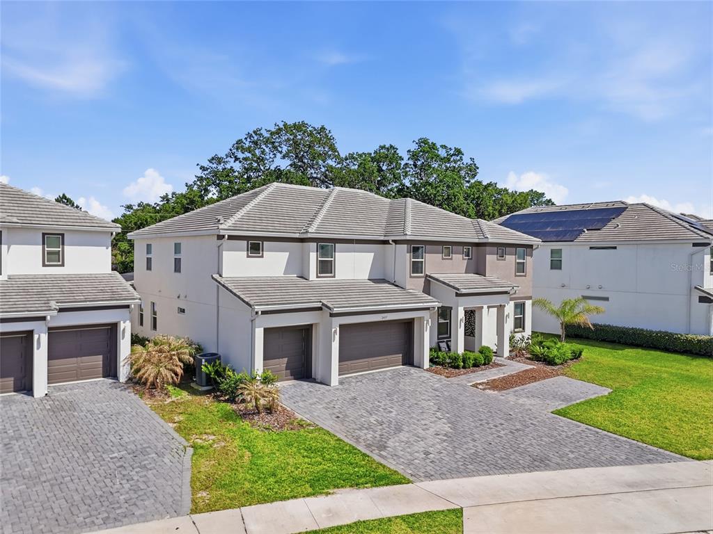 An exterior view of a two-story suburban house with a paver driveway and attached garages — 2437 SHANTI DRIVE, KISSIMMEE, FL