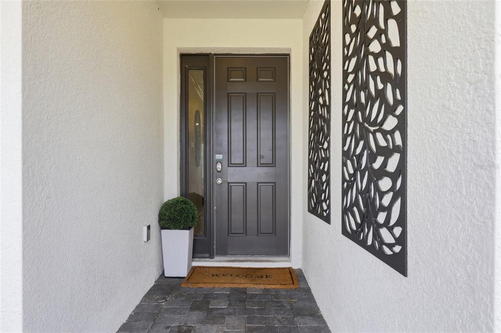 A dark gray front door with a side window sits at the end of a porch — 2437 SHANTI DRIVE, KISSIMMEE, FL