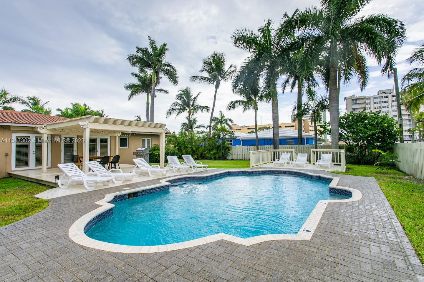 A backyard features a swimming pool, a patio with lounge chairs, and a wooden pergola — 714 Harrison St, Hollywood FL 33019, HOLLYWOOD, FL