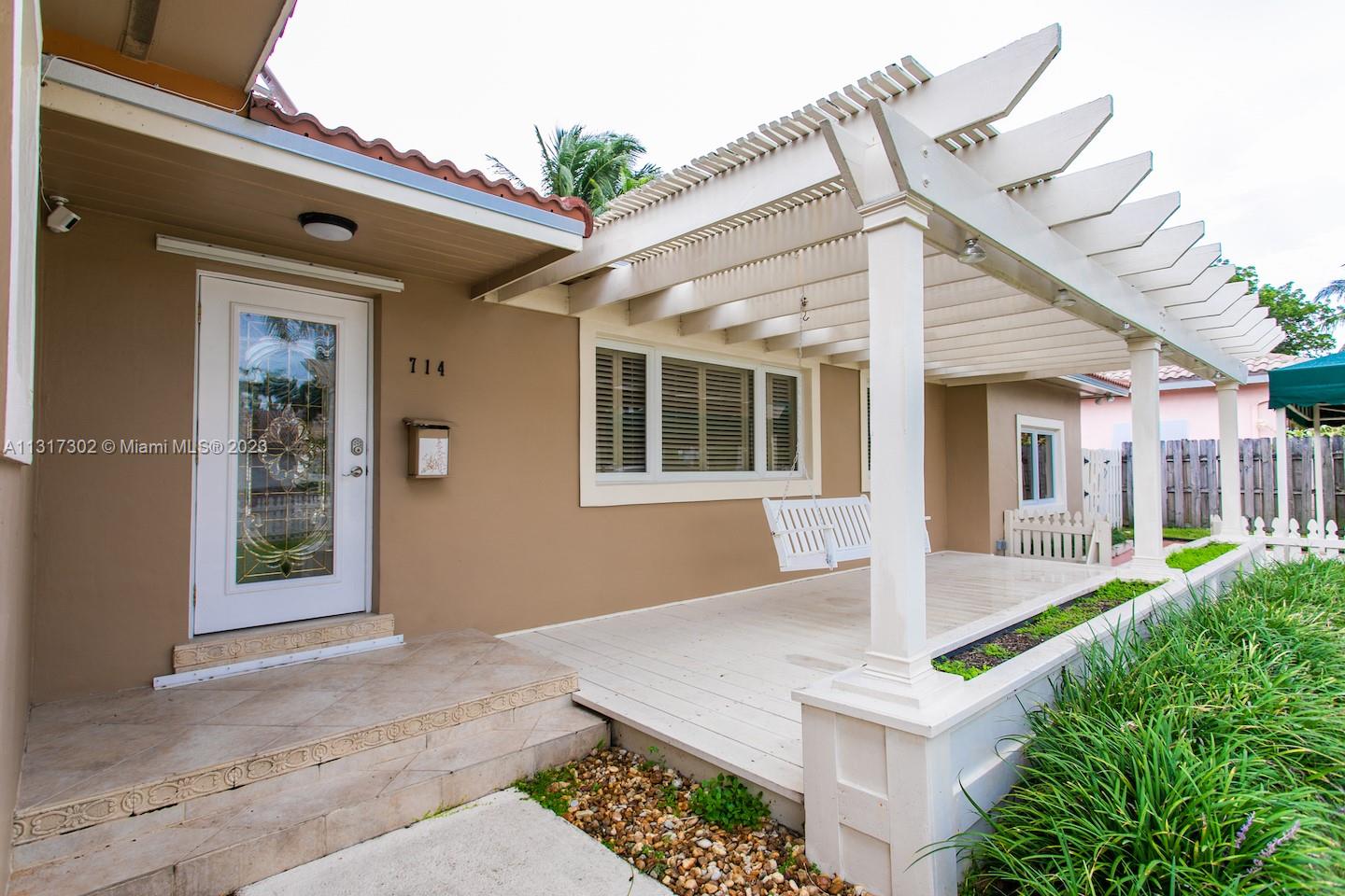 A house exterior features a front door, a covered wooden porch, and a white pergola — 714 Harrison St, Hollywood FL 33019, HOLLYWOOD, FL