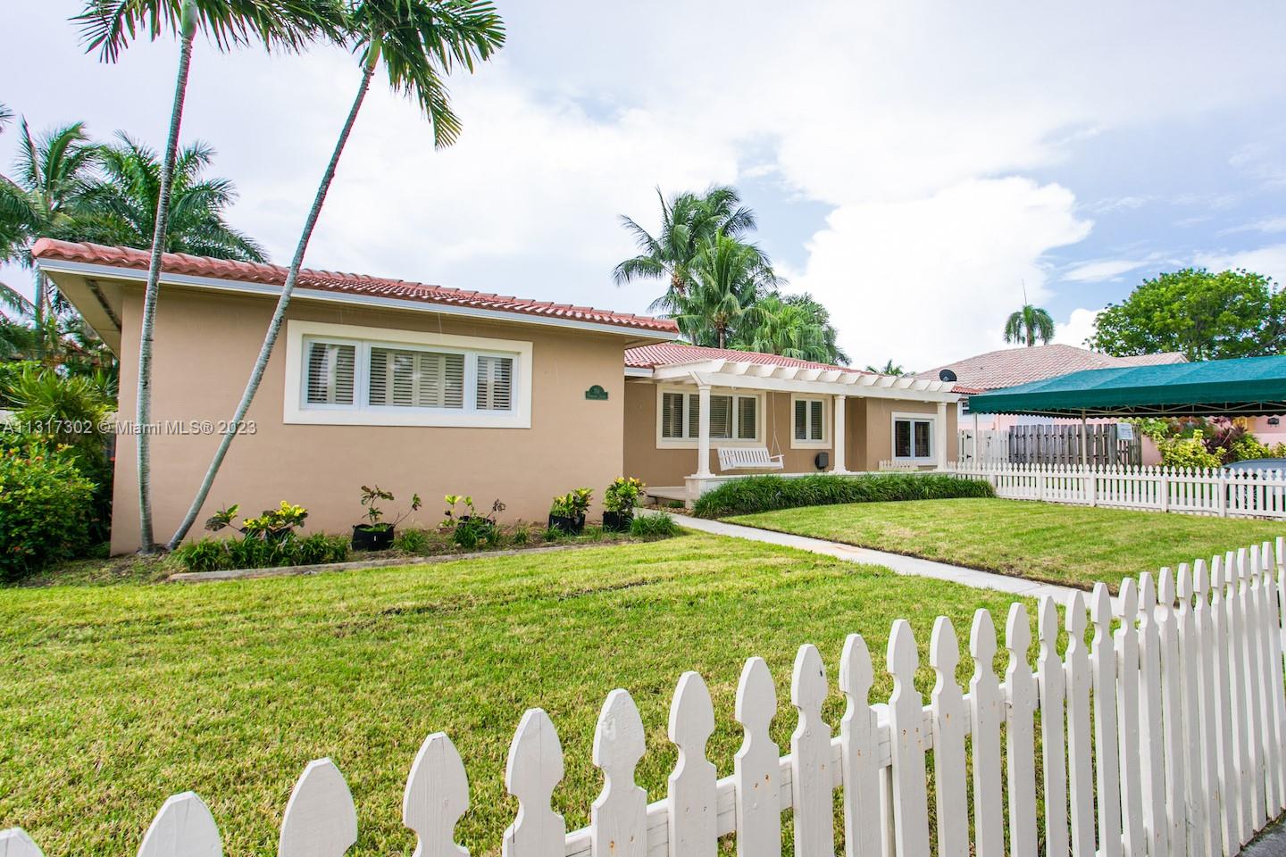 A tan single-story house features a white picket fence, a pergola, and palm trees — 714 Harrison St, Hollywood FL 33019, HOLLYWOOD, FL