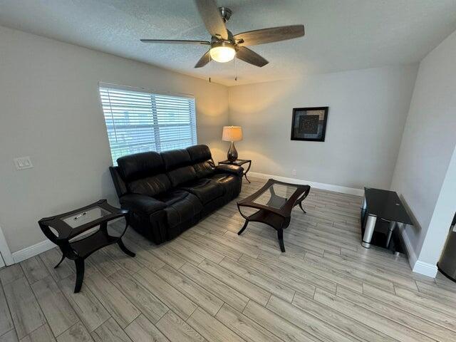 A living room features a black leather sofa, glass-topped tables, and light wood-look flooring — 127 Flanders # C, Delray Beach FL 33484, DELRAY BEACH, FL