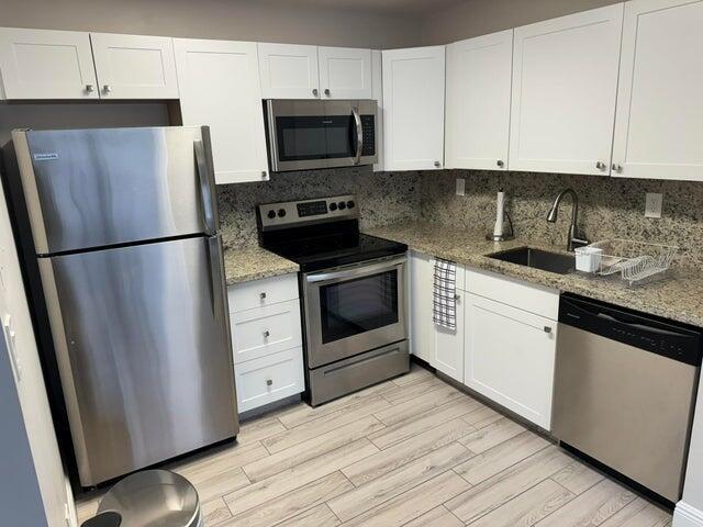 A kitchen features white cabinets, stainless steel appliances, granite countertops, and light wood-look flooring — 127 Flanders # C, Delray Beach FL 33484, DELRAY BEACH, FL