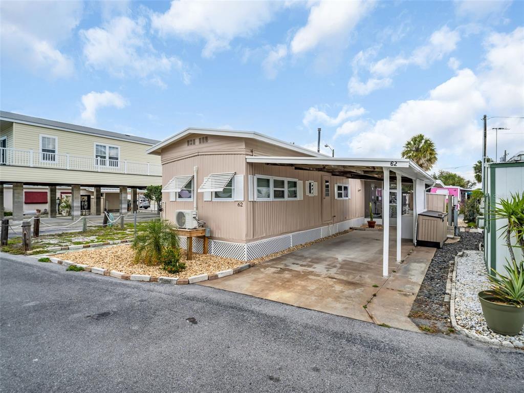 A tan mobile home with a carport and gravel landscaping sits under a cloudy sky — 800 CHESAPEAKE DRIVE UNIT 62, TARPON SPRINGS, FL