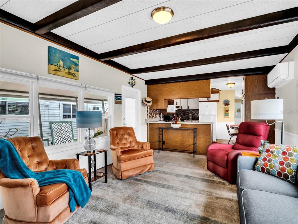 A living room with wood-beamed ceilings, two brown armchairs, a red recliner, and an open kitchen — 800 CHESAPEAKE DRIVE UNIT 62, TARPON SPRINGS, FL