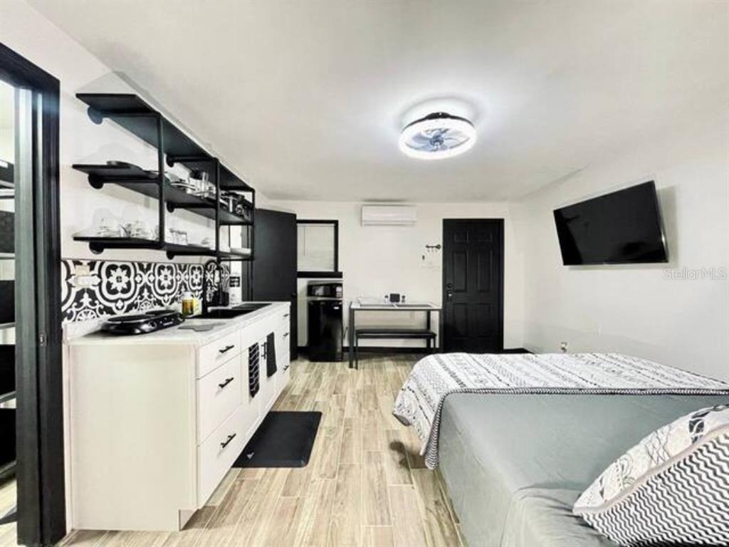 A studio apartment features a kitchenette with open shelving, a bed, and a wall-mounted television — 1731 GRAYSON DR UNIT 3, ORLANDO, FL