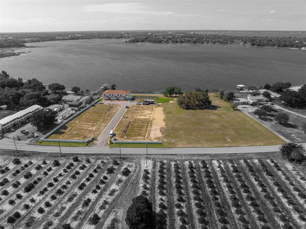 An aerial view shows a vacant waterfront lot next to a residential building and orchard — 1877 ARBUCKLE CREEK ROAD, SEBRING, FL
